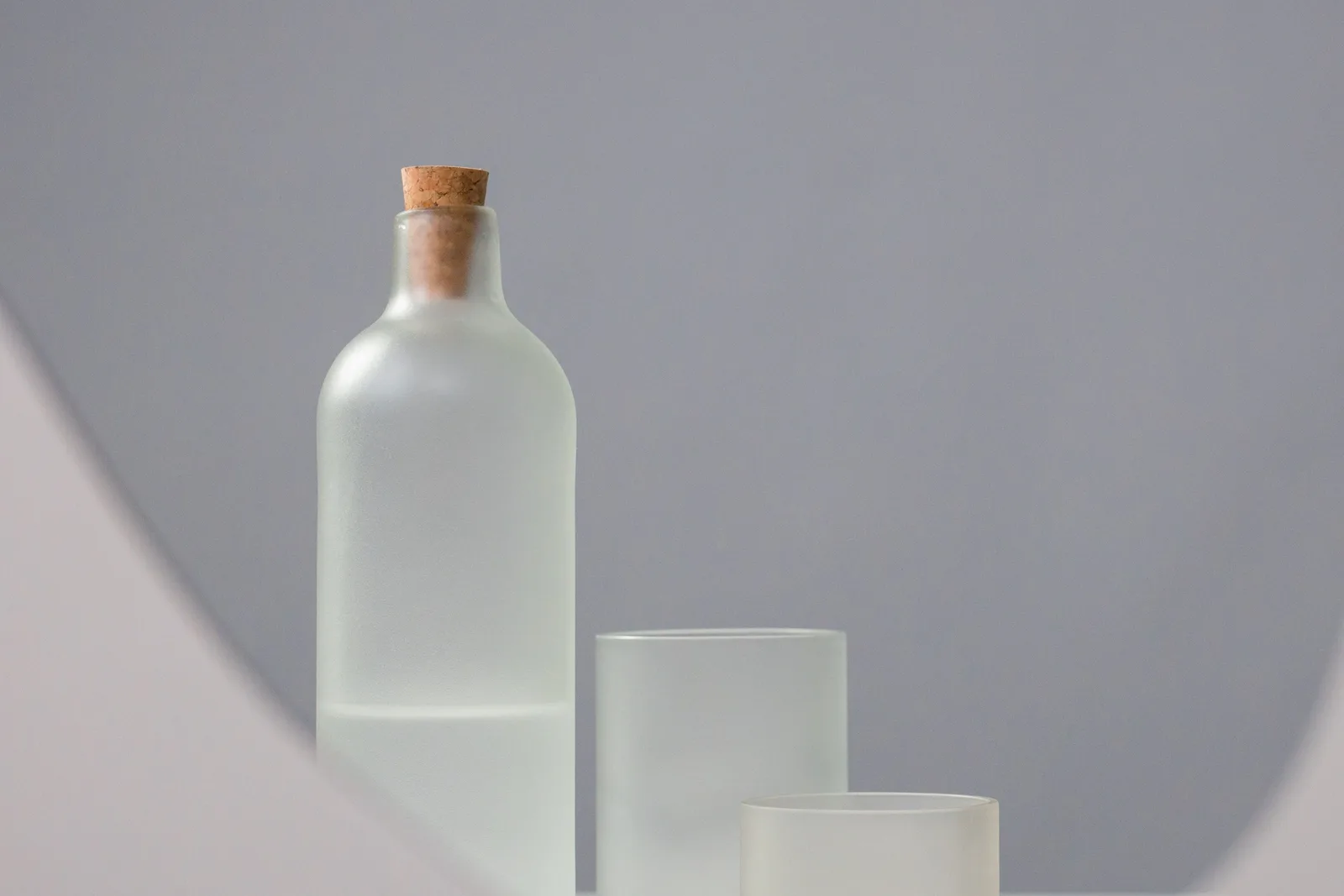 Glass bottle with a cork stopper and two glasses on a calm grey background