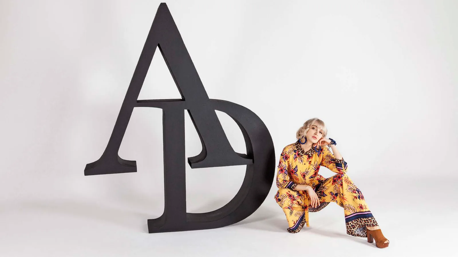AD Magazine fashion editorial — model in yellow paisley dress beside giant A_D typographic sculpture