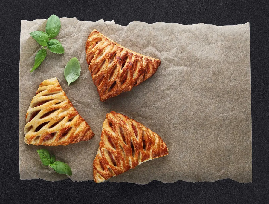 Food photography — triangular pastry products on kraft paper, dark background, bakery commercial