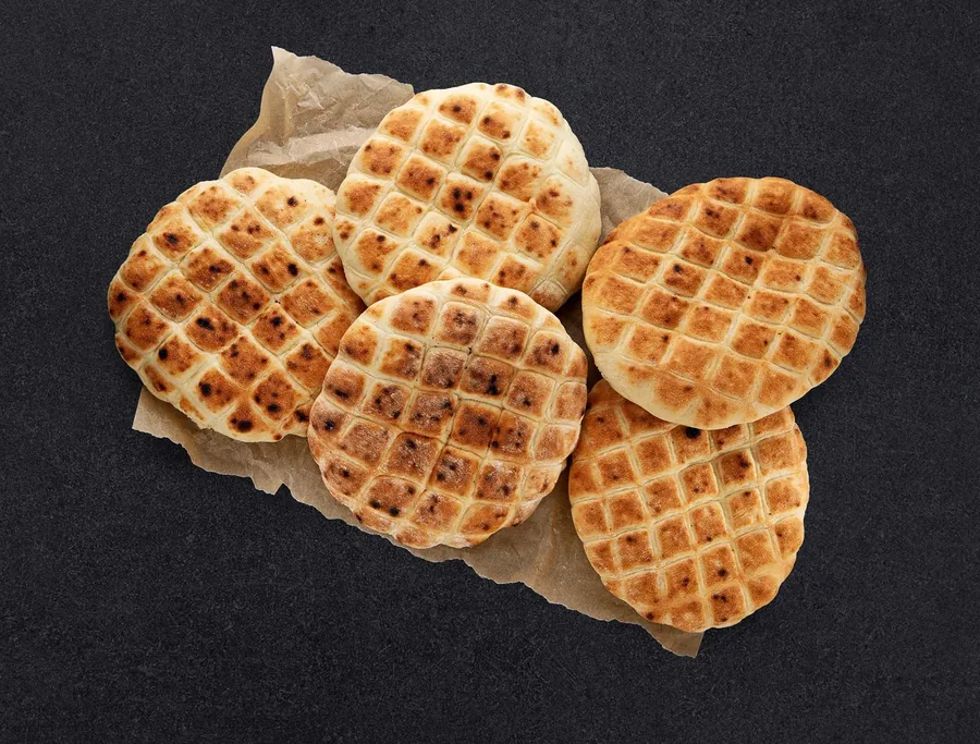Food photography — waffle-pattern flatbreads on kraft paper, dark background, bakery product shot