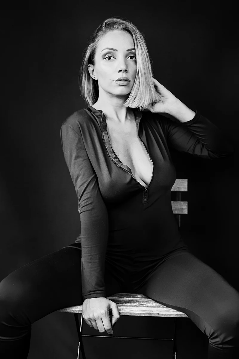 Studio portrait Zagreb — woman in black bodysuit seated on box, dramatic black and white lighting
